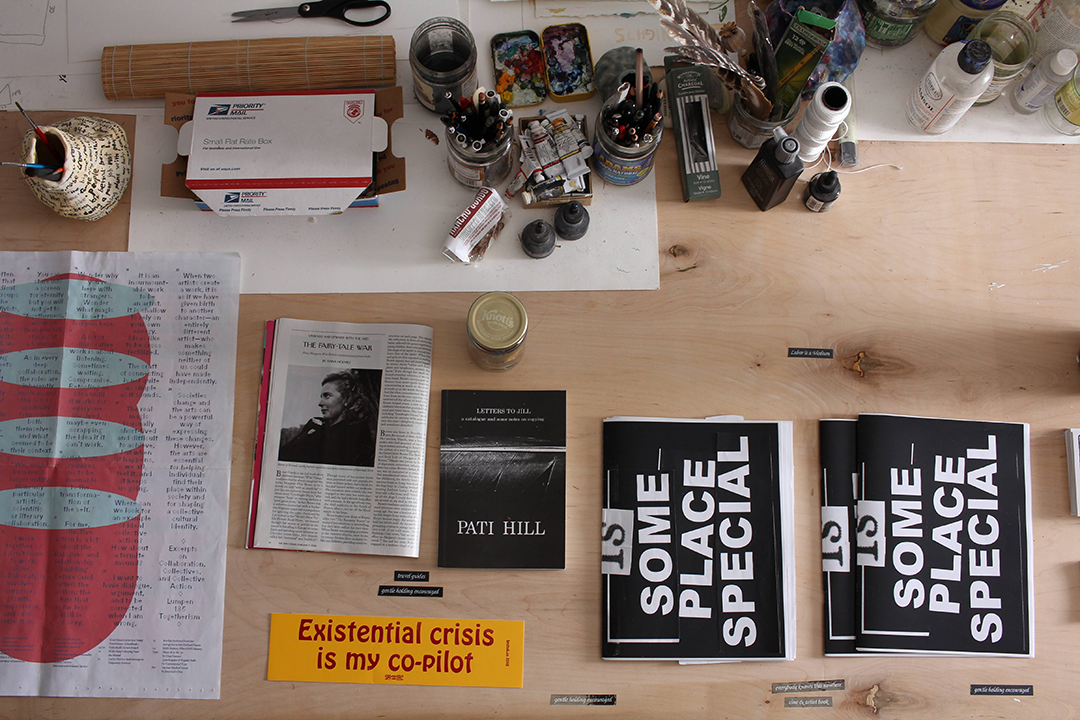 A table with various print ephemera including a magazine, a bumber sticker that says existential crisis is my co-pilit, and a booklet that says some place special.
