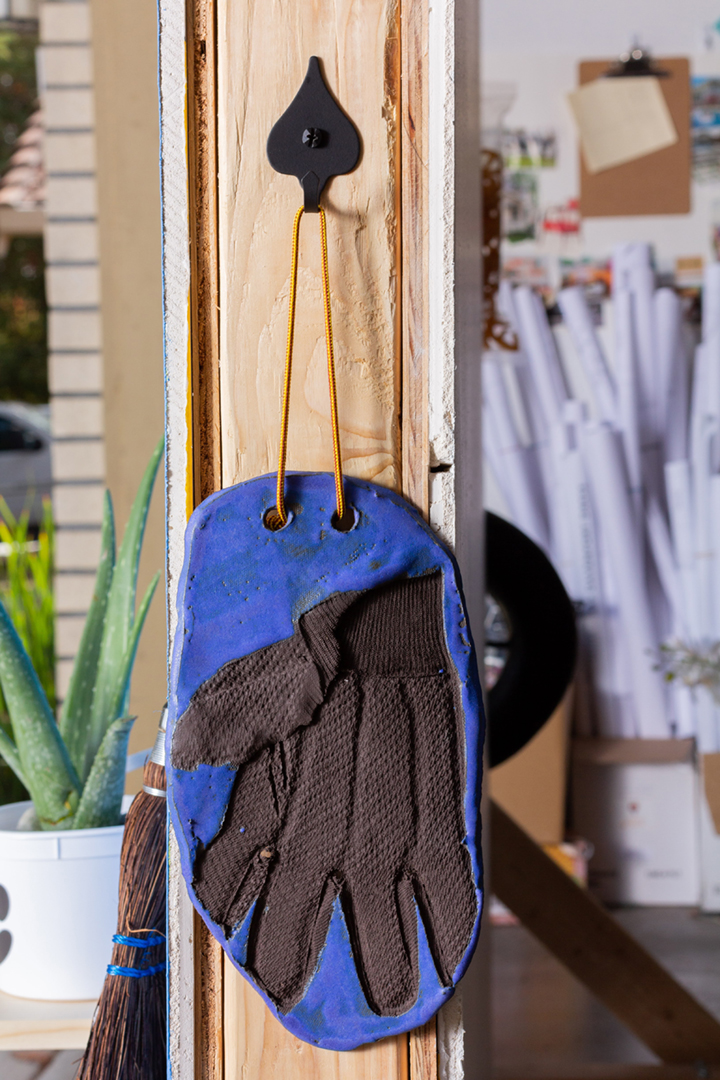 A blue wall with several objects including a wooden bench, silver milagros, a cassette player, paintings of candles, an aloe plant, tools, and more.