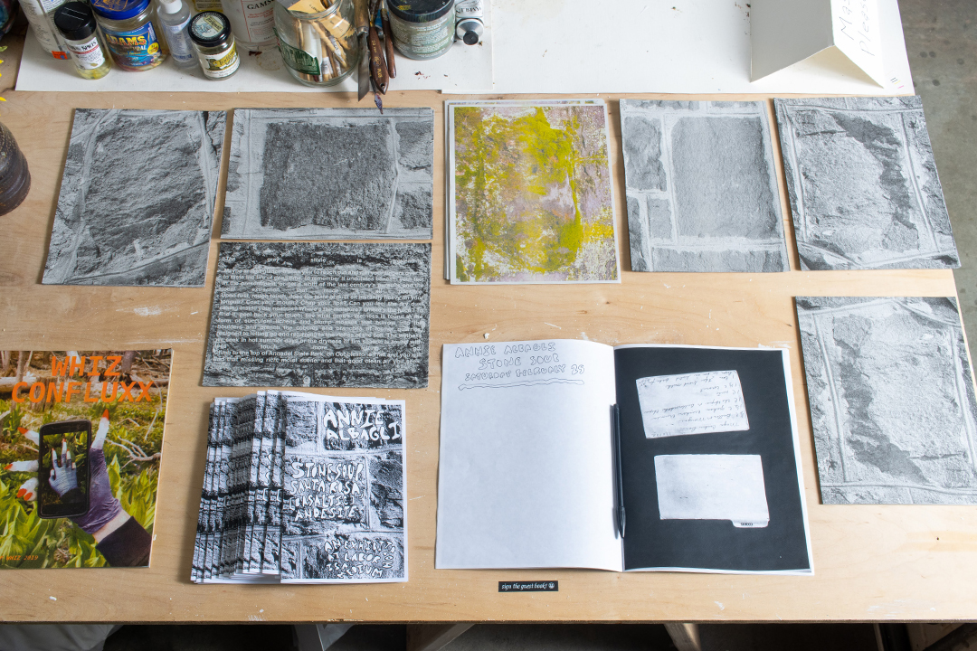 A table with stacks of grey paper printed with images of stones, along with an open guest bbook and other ephemera