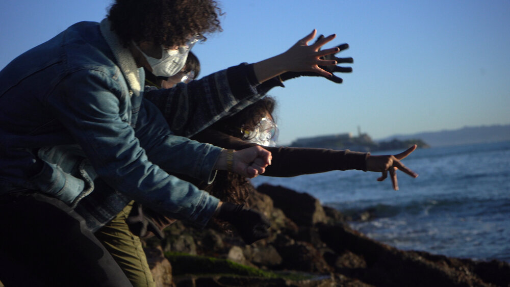 People wearing n95 masks reaching out toward the ocean